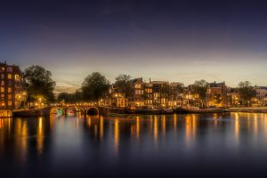 Evening scene of the river Amstel at blue hour, illuminated houses and bridges, Amsterdam, Netherlands